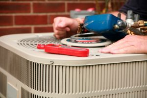 technicians hands with tools on top of ac outside unit