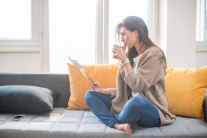 young-woman-sitting-indoors-looking-at-computer-and-reading-tablet