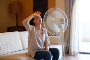 woman-sitting-on-couch-with-hand-to-forehead-while-sitting-in-front-of-box-fan